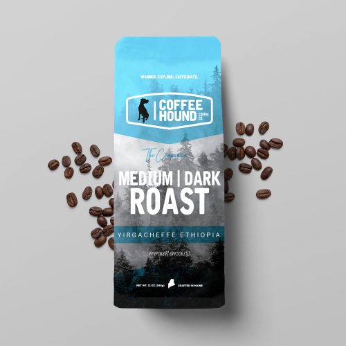 Bag of Coffee Hound Medium Roast Small-Batch Craft Coffee, featuring sleek packaging and a rustic wooden background with scattered coffee beans and a steaming cup of coffee.